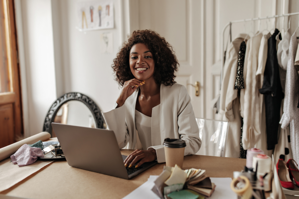 charming-young-darkskinned-woman-stylish-jacket-blouse-smiles-looks-camera-works-laptop-poses-office